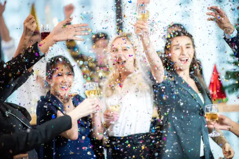 Eine Gruppe von Menschen feiert ausgelassen mit buntem Konfetti und Sekt – NAR Kitchen bietet das passende vegane Catering für unvergessliche Geburtstagsfeiern