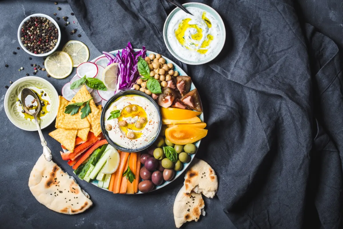 Mediterranes veganes Catering: Buntes Arrangement aus cremigem Hummus, Oliven, Pistazien und gefüllten Minipaprika von NAR Kitchen