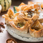 Pflanzliches Dessert-Highlight: Cremige Cheesecake-Füllung trifft auf knusprige Baklava-Elemente und gehobelte Mandeln – kreiert von NAR Catering